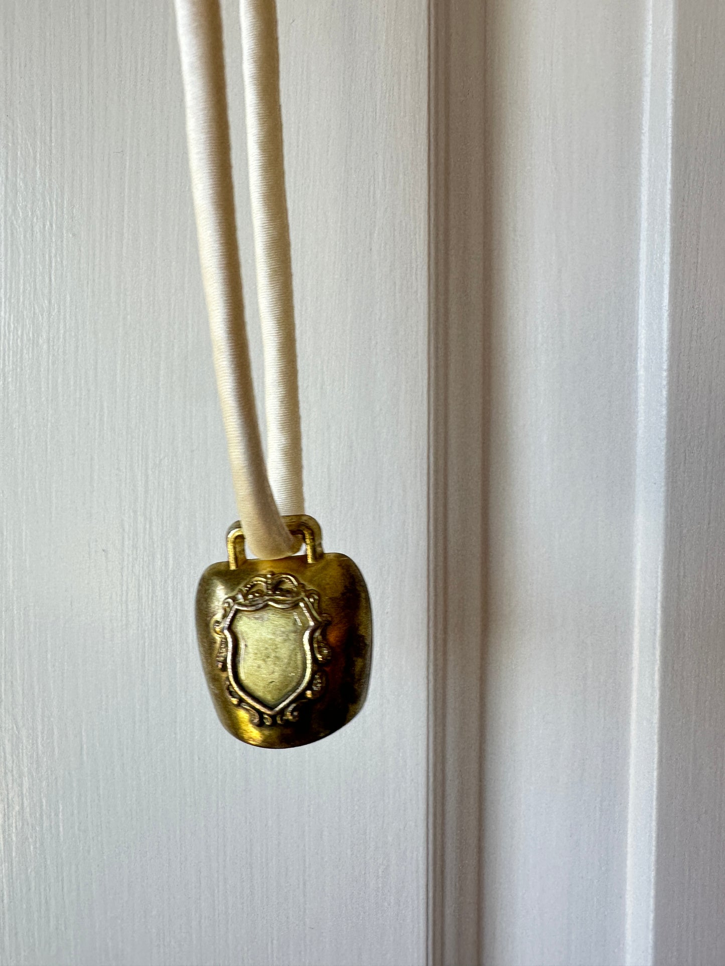 Artisanal mini brass bell pendant on off white silk cord
