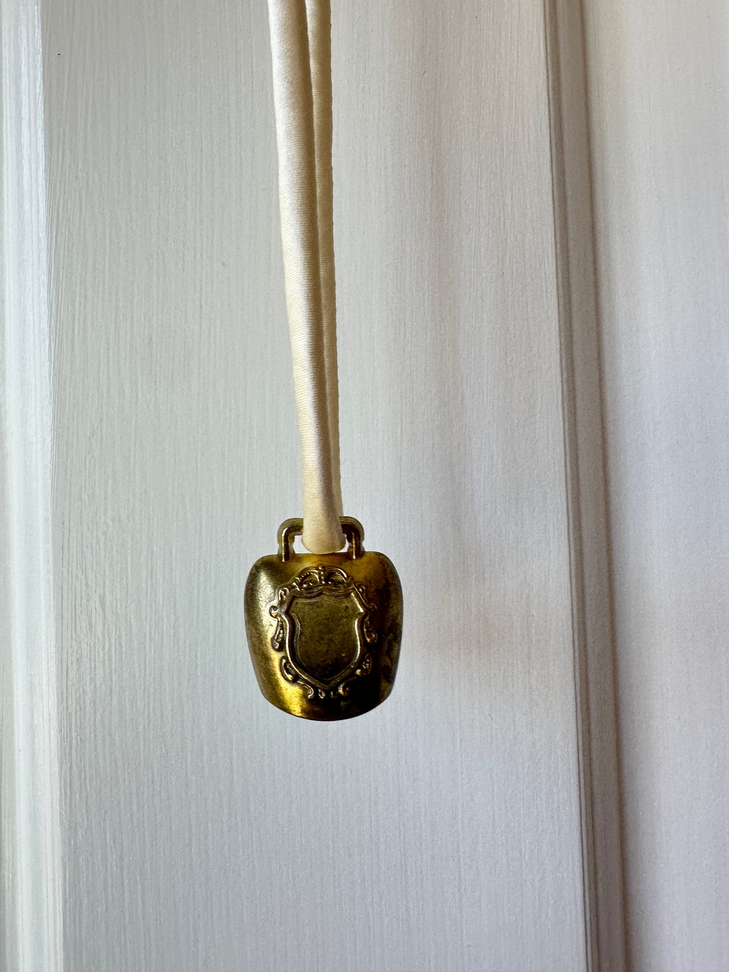 Artisanal mini brass bell pendant on off white silk cord