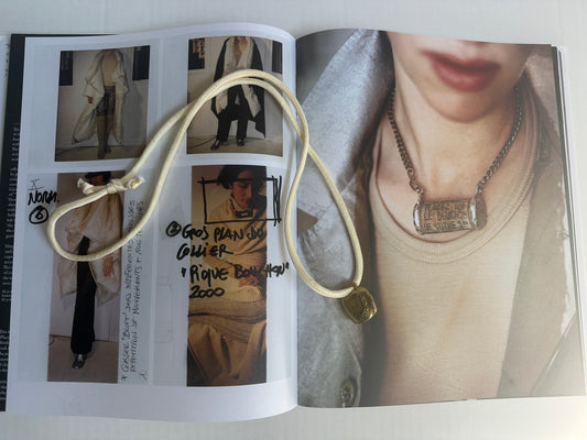 Artisanal mini brass bell pendant on off white silk cord