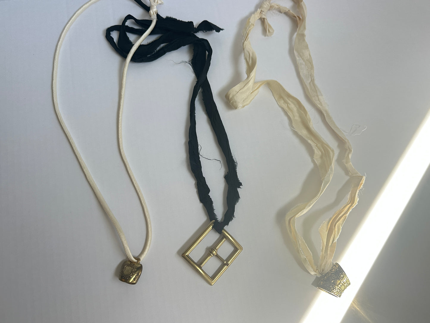 Artisanal mini brass bell pendant on off white silk cord