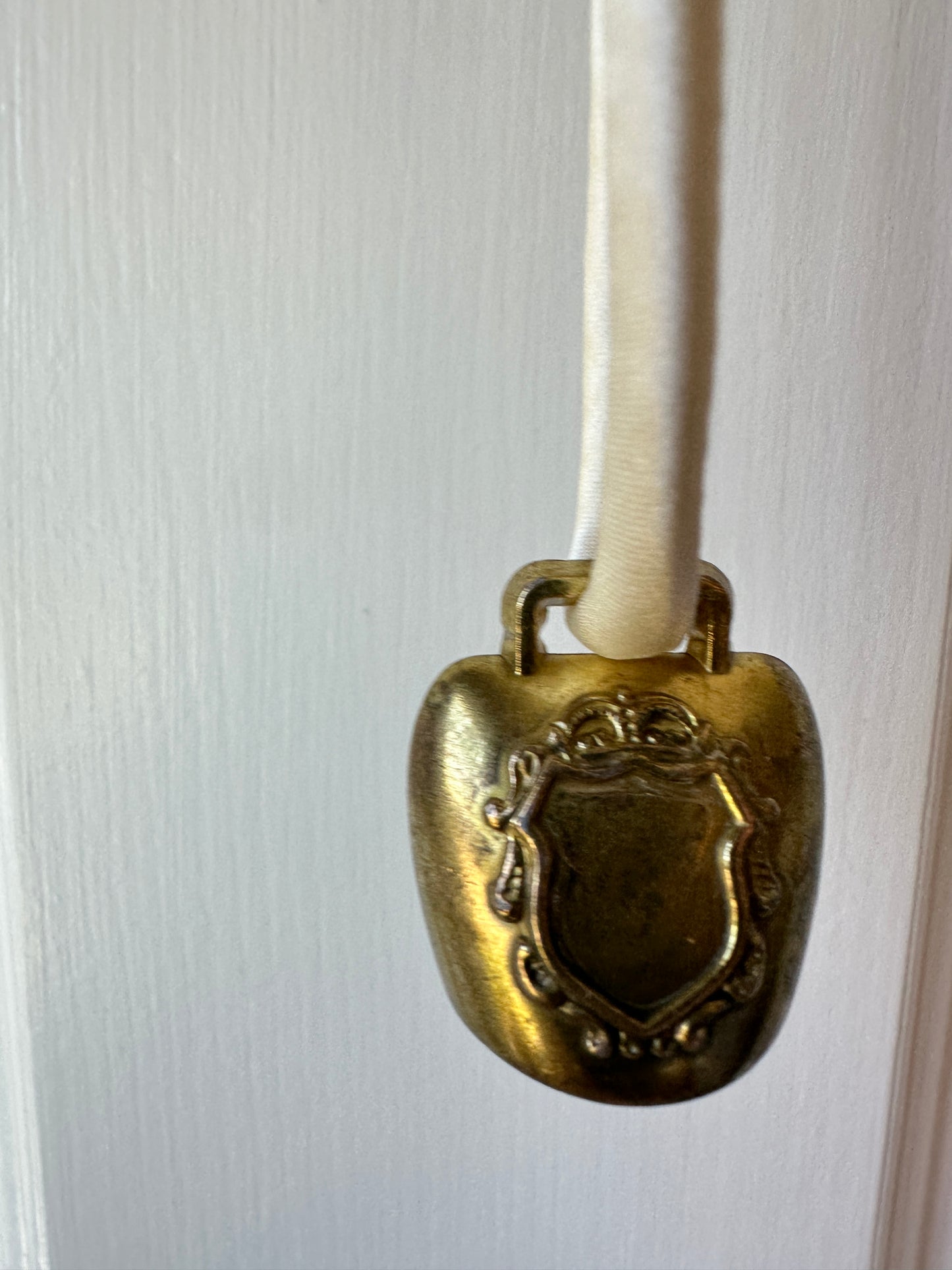 Artisanal mini brass bell pendant on off white silk cord