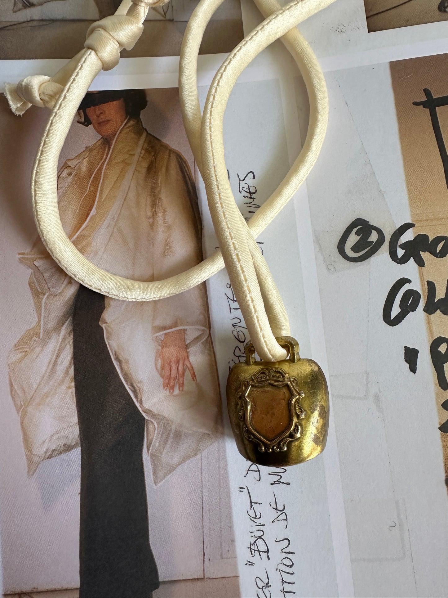 Artisanal mini brass bell pendant on off white silk cord