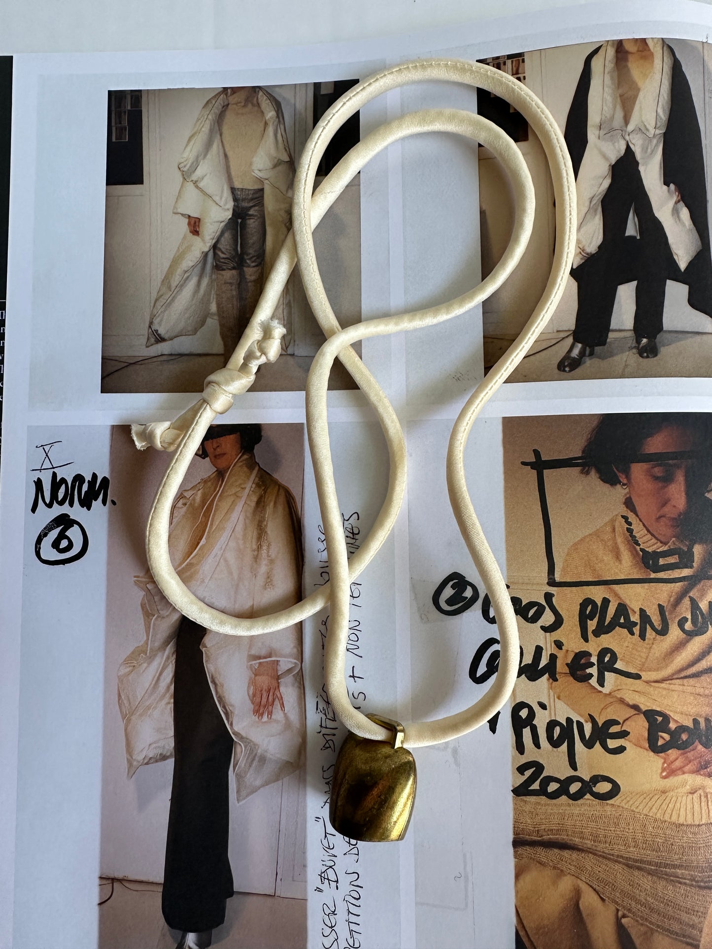Artisanal mini brass bell pendant on off white silk cord