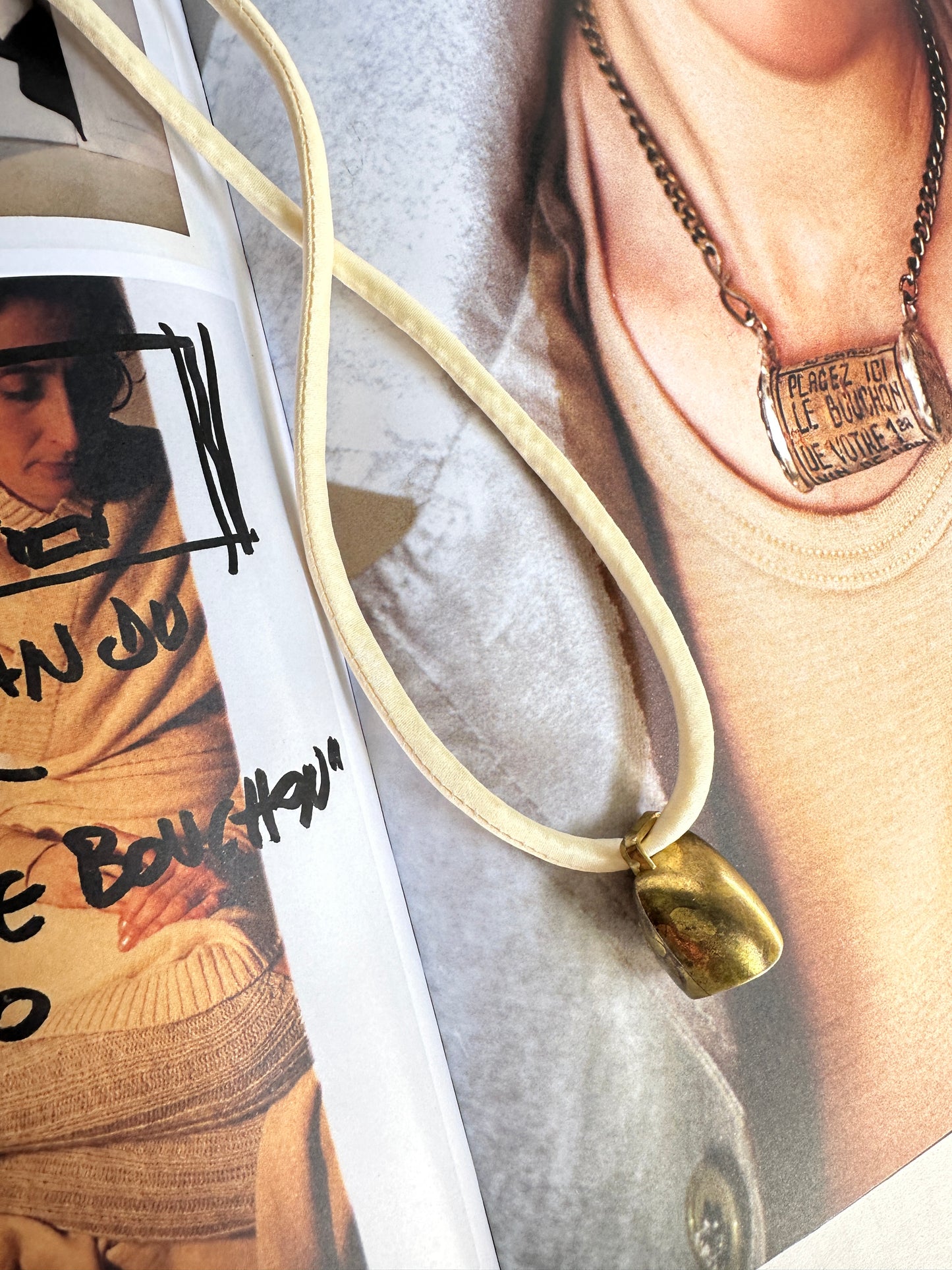 Artisanal mini brass bell pendant on off white silk cord