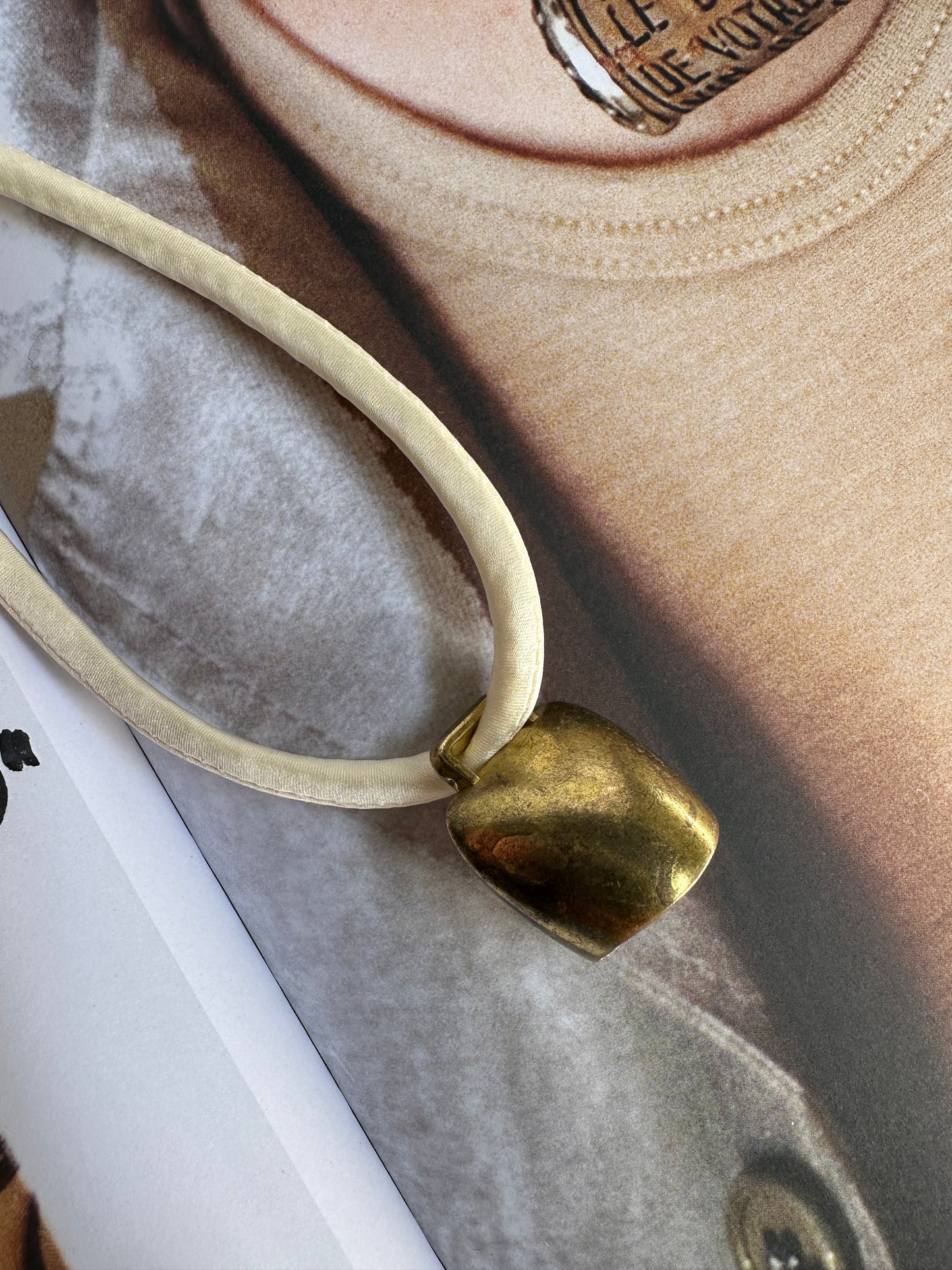 Artisanal mini brass bell pendant on off white silk cord