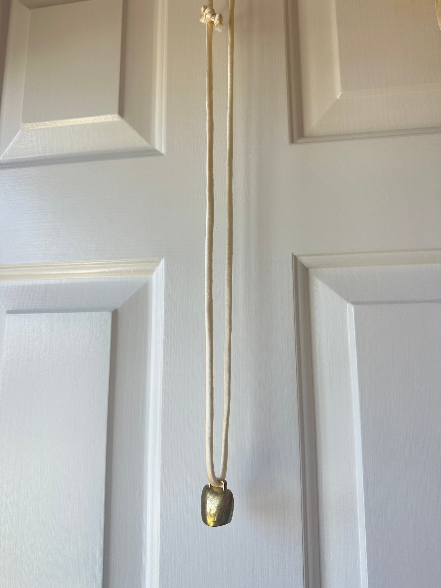 Artisanal mini brass bell pendant on off white silk cord