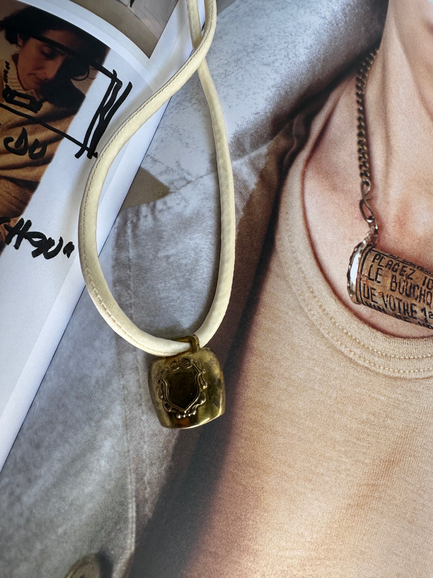 Artisanal mini brass bell pendant on off white silk cord