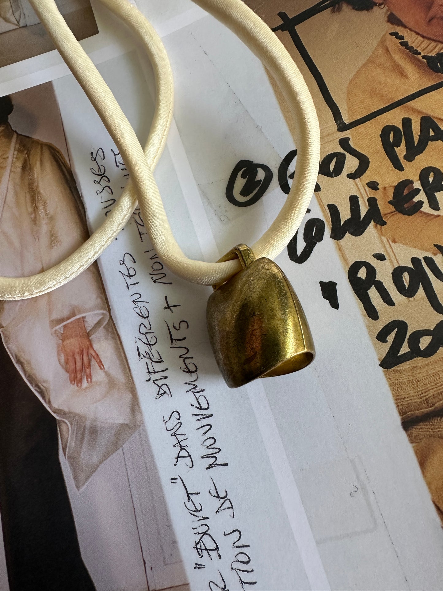Artisanal mini brass bell pendant on off white silk cord
